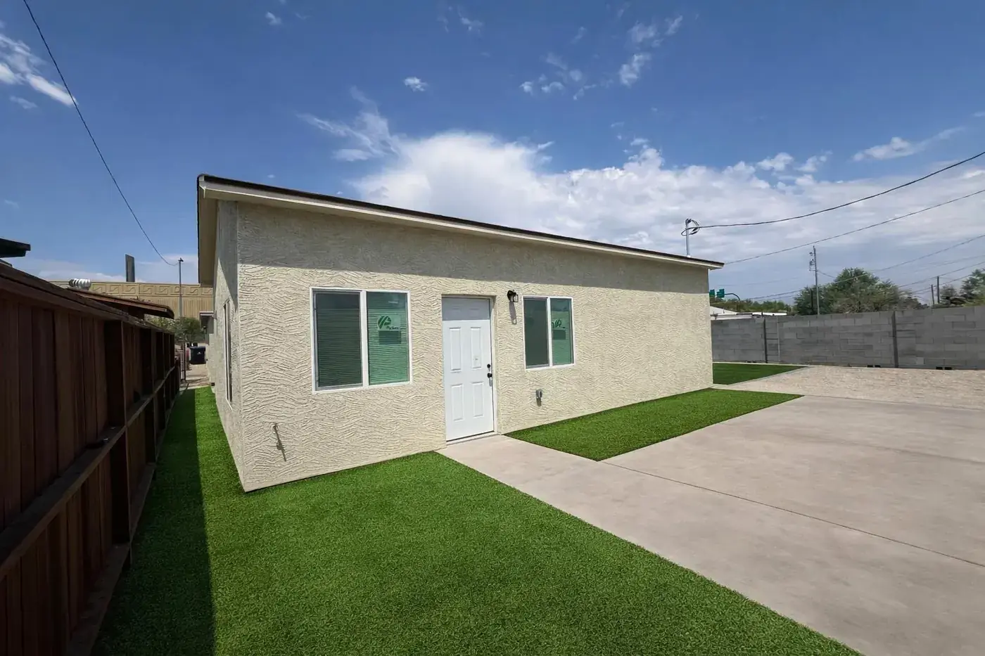 The finished 900 square foot casita in Phoenix, with stucco walls, a white front door and turf either side of a concrete path.