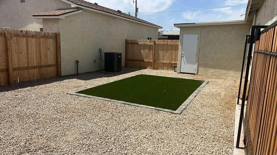 Gravel yard with a turf pad, wooden fence and an air conditioning condenser beside the casita.