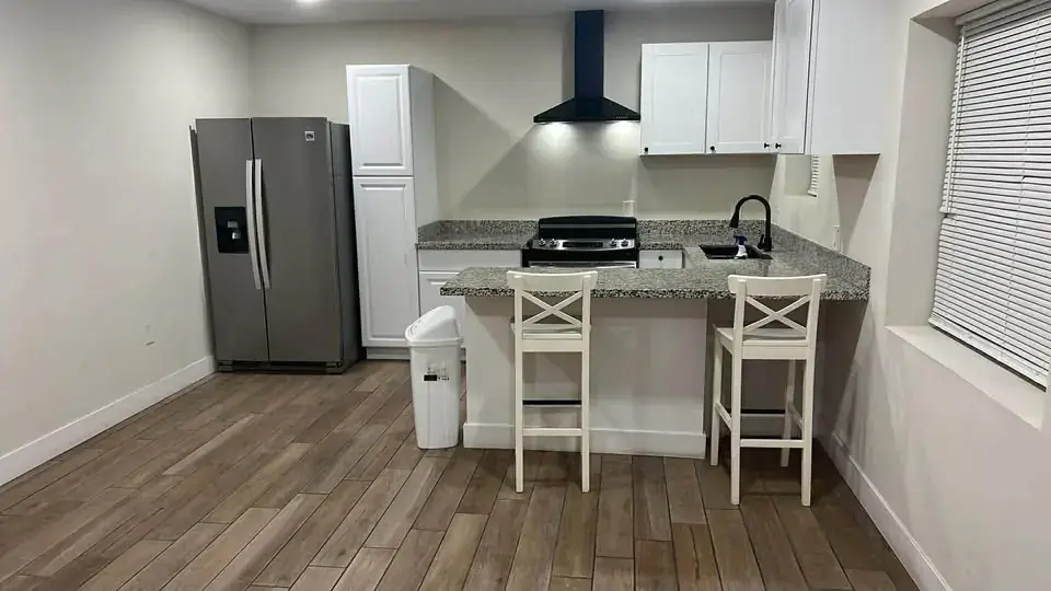 Kitchen with white cabinets, granite counters, stainless fridge, range and a breakfast bar with two stools.