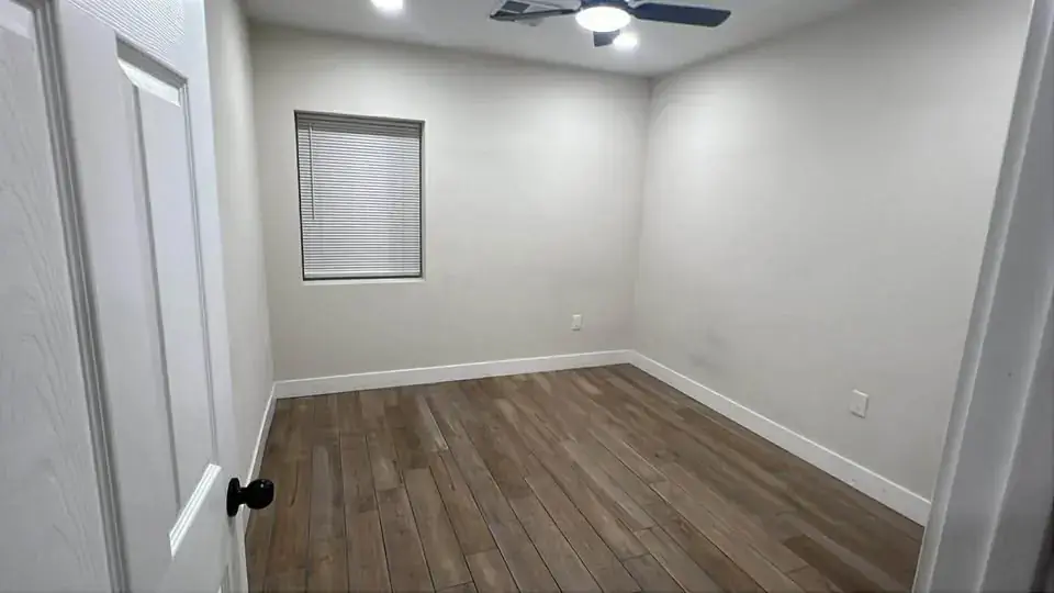 Empty main bedroom with wood-look tile floor, ceiling fan and a window with blinds.