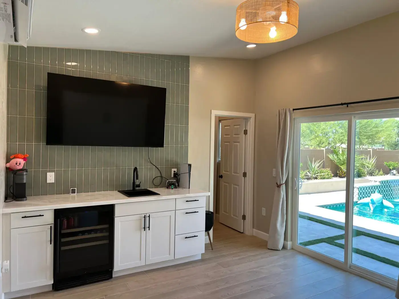 Kitchenette with white cabinets, sink, beverage fridge and a wall-mounted television.