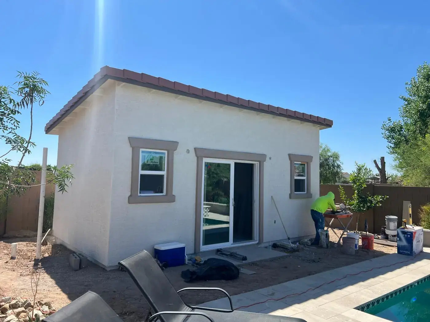 Stuccoed casita with sliding glass door installed and a worker cutting tile outside.