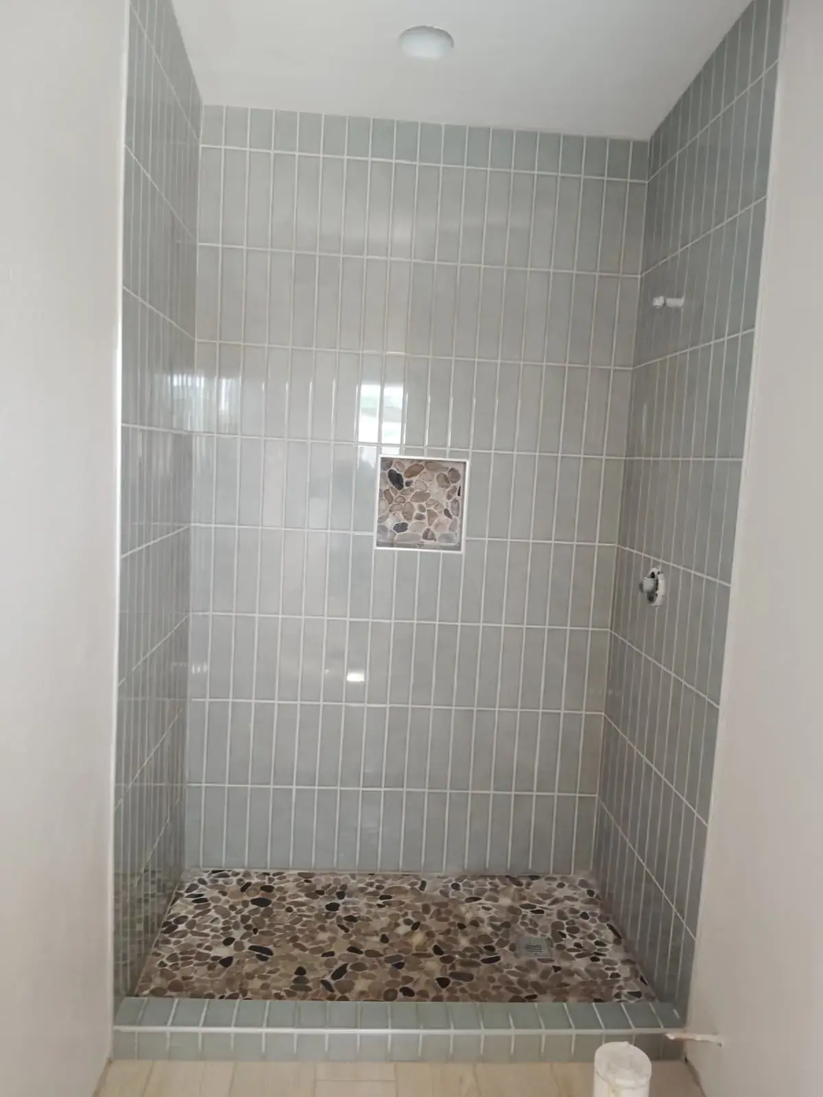 Tiled shower alcove with green stacked tile and a pebble floor, before the glass was fitted.